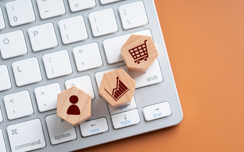 Wooden blocks imprinted with symbols for shopping online sit on keyboard. Learn when it's time to outsource your copywriting to boost your sales from WhitneyWroteThis.com.